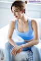 A woman in a blue sports bra top sitting on a bed.