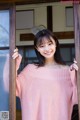 A woman in a pink sweater leaning against a window.