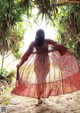 A woman in a long dress walking on a sandy beach.