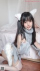 A woman in a gray sweater and white stockings sitting on a bed.
