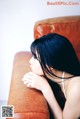 A woman sitting on a brown couch with her hand on her chin.