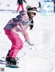 A young girl is snowboarding down a snowy hill.