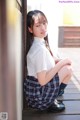 A young woman in a school uniform leaning against a wall.