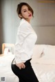 A woman in a white shirt and black pants posing on a bed.