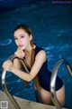 A woman in a black bathing suit leaning on the edge of a swimming pool.