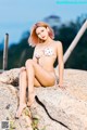 A woman in a white bikini sitting on a rock.