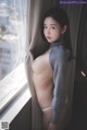 A naked asian woman leaning against a window.