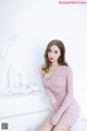 A woman in a pink dress sitting on a white dresser.