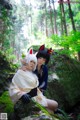 A couple of women sitting on top of a rock in the woods.